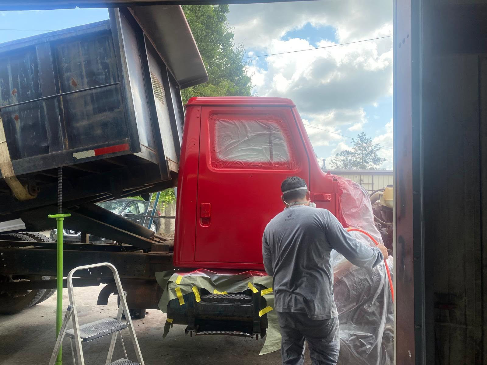 Technician spraying fresh red paint on a dump truck cab inside the shop